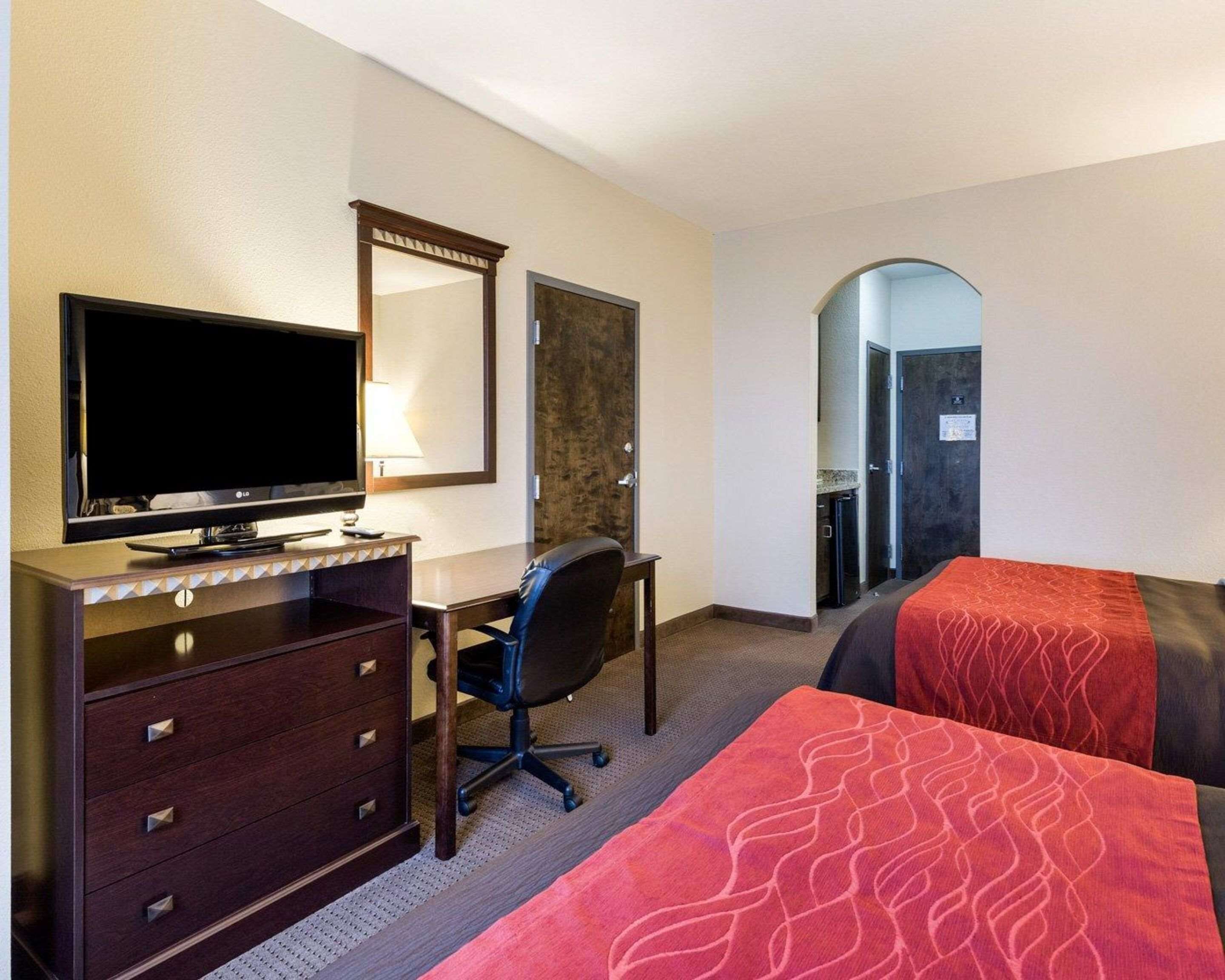 A hotel room with a desk, a flat-screen TV, a chair, two beds, a mirror, and a door leading to a bathroom.
