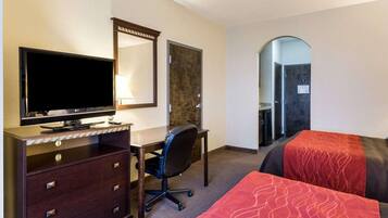 A hotel room with a desk, a flat-screen TV, a chair, two beds, a mirror, and a door leading to a bathroom.