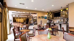 Un restaurant avec des tables et des chaises rondes, un coin bar et un escalier menant à un étage supérieur.