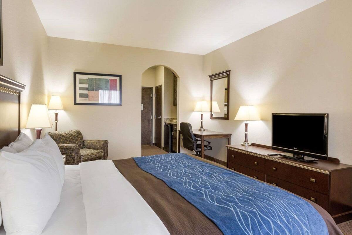Ein Hotelzimmer mit einem großen Bett, einem Schreibtisch mit Stuhl, einem Fernseher und zwei Lampen.