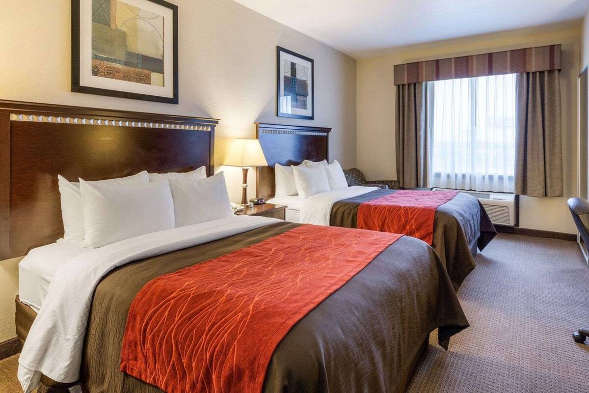 Ein Hotelzimmer mit zwei Betten, einem großen Fenster mit Vorhängen und einem gerahmten Bild an der Wand.