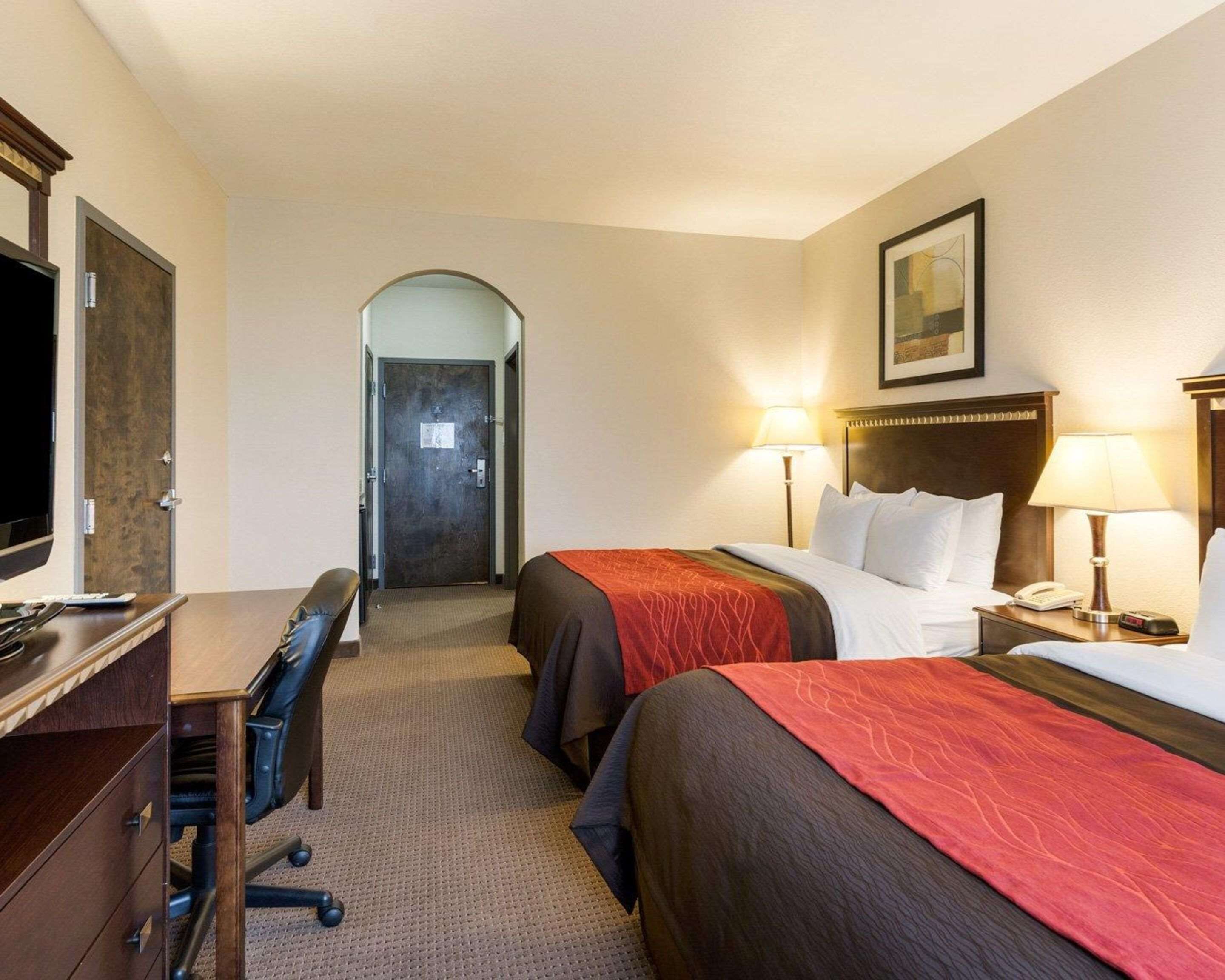 A hotel room with two beds, a desk, a chair, a TV, and a door leading to another room.