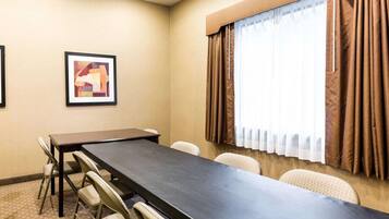 A conference room with a long table and six chairs, a framed abstract painting on the wall, and a window with brown curtains.
