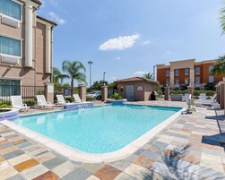 Piscina con sillas de descanso y un pequeño edificio, rodeado por una cerca y palmeras.