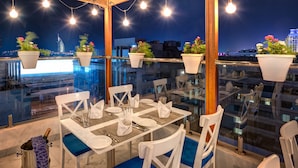 A rooftop dining area with tables set for four, potted plants, and a view of the city skyline at night. - Donatello Hotel (Dubai)