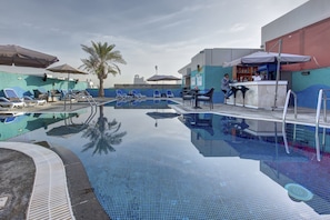 A swimming pool with lounge chairs and umbrellas, a bar area, and a palm tree. - Donatello Hotel (Dubai)