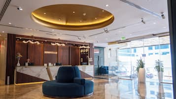 Un espace d’accueil d’hôtel avec un comptoir en marbre, un fauteuil bleu et un grand luminaire circulaire au plafond.