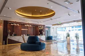 A hotel reception area with a marble counter, a blue armchair, and a large circular ceiling light. - Donatello Hotel (Dubai)