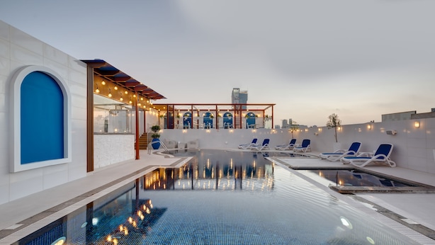 A rooftop infinity pool with lounge chairs, a covered seating area, and a modern architectural design. - Donatello Hotel (Dubai)