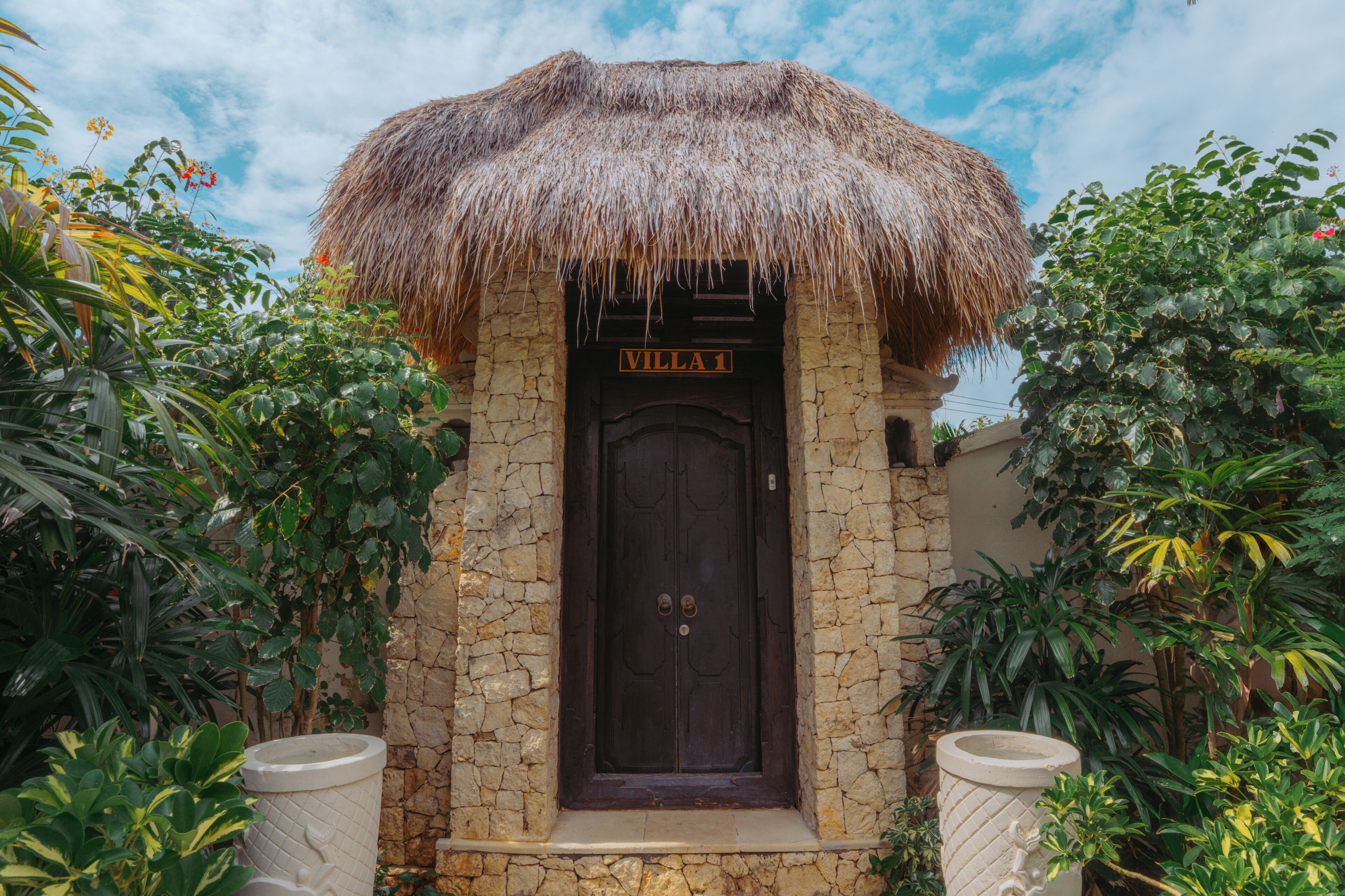 Une villa en pierre avec un toit de chaume, une porte en bois sombre et une enseigne indiquant « Villa 1 ».