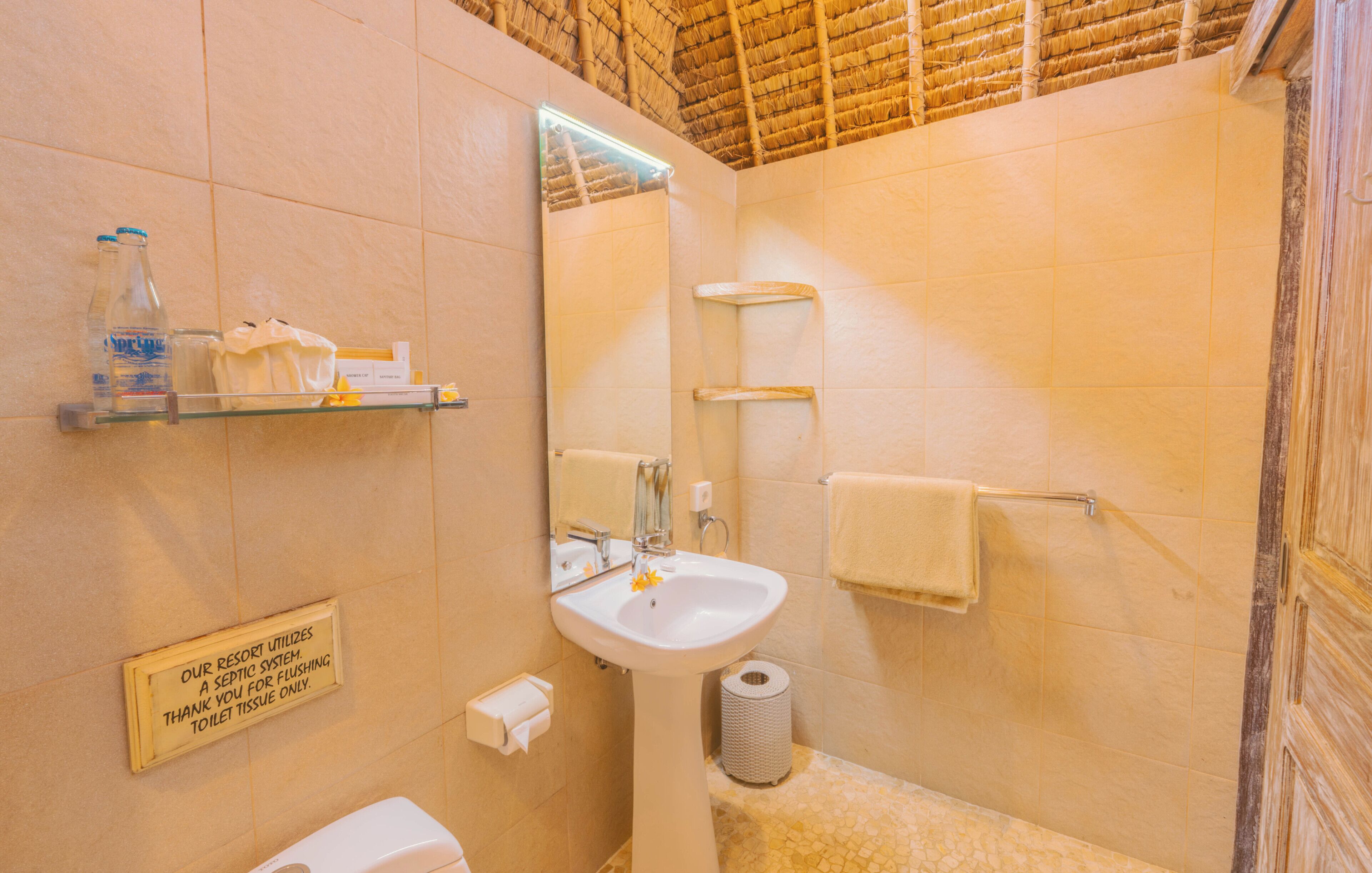 Un baño con lavamanos, espejo, toallero y un cartel sobre el sistema séptico del resort.