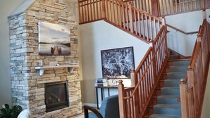 A spacious living area with a stone fireplace, wooden staircase, and a chandelier. - GrandStay Hotel & Suites Perham (Perham)