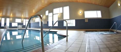 Una piscina interior con agua cristalina, suelo de baldosas y techo de madera.