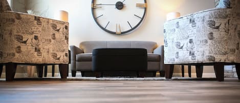 A living room with a round wall clock, two patterned armchairs, a sofa, and a coffee table.