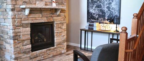 Una chimenea de piedra con repisa, una escalera de madera y un comedor con mesa y sillas.
