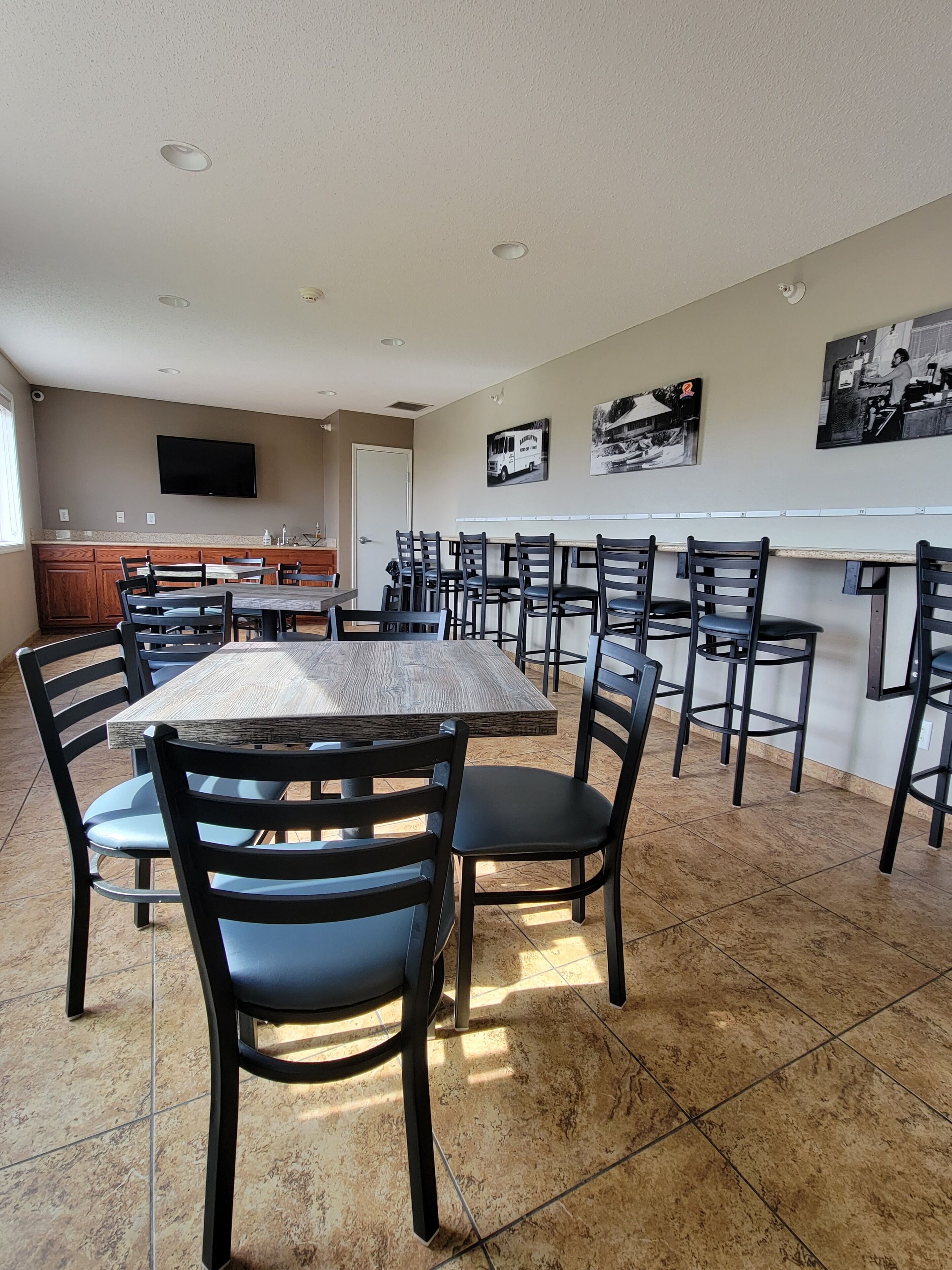 A dining area with a long table and multiple chairs, a kitchen area with a sink and cabinets, and a television mounted on the wall.