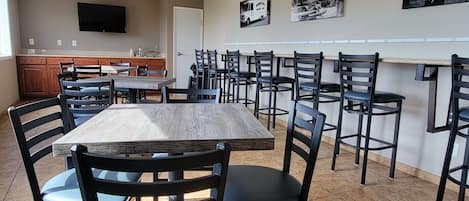 A dining area with a long table and multiple chairs, a kitchen area with a sink and cabinets, and a television mounted on the wall.