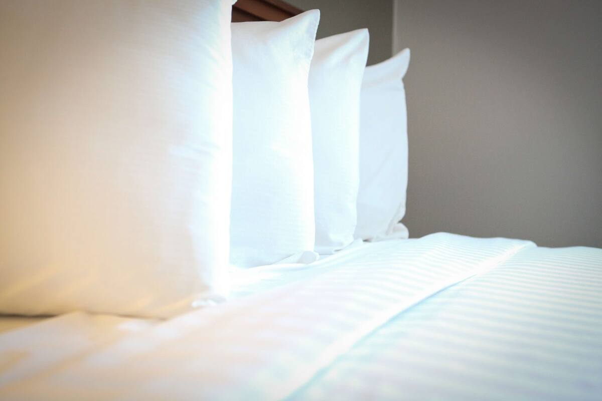 A neatly made bed with white linens and pillows.