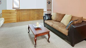 A living room with a wooden cabinet, a black leather sofa, and a wooden coffee table with a lit candle. - Knights Inn Muskogee (Muskogee)