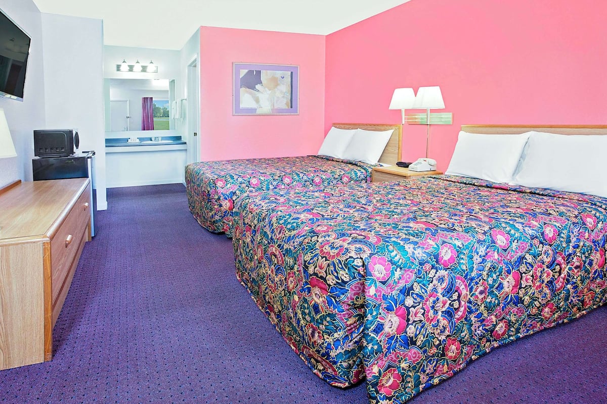 A hotel room with two beds, a desk, a TV, and a bathroom visible through an open door.