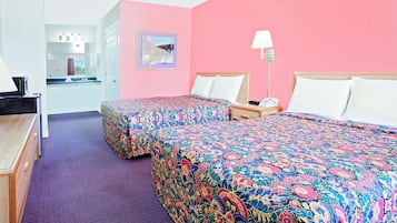 Habitación de hotel con dos camas, un escritorio, una silla, una lámpara y un baño a la vista a través de una puerta abierta.
