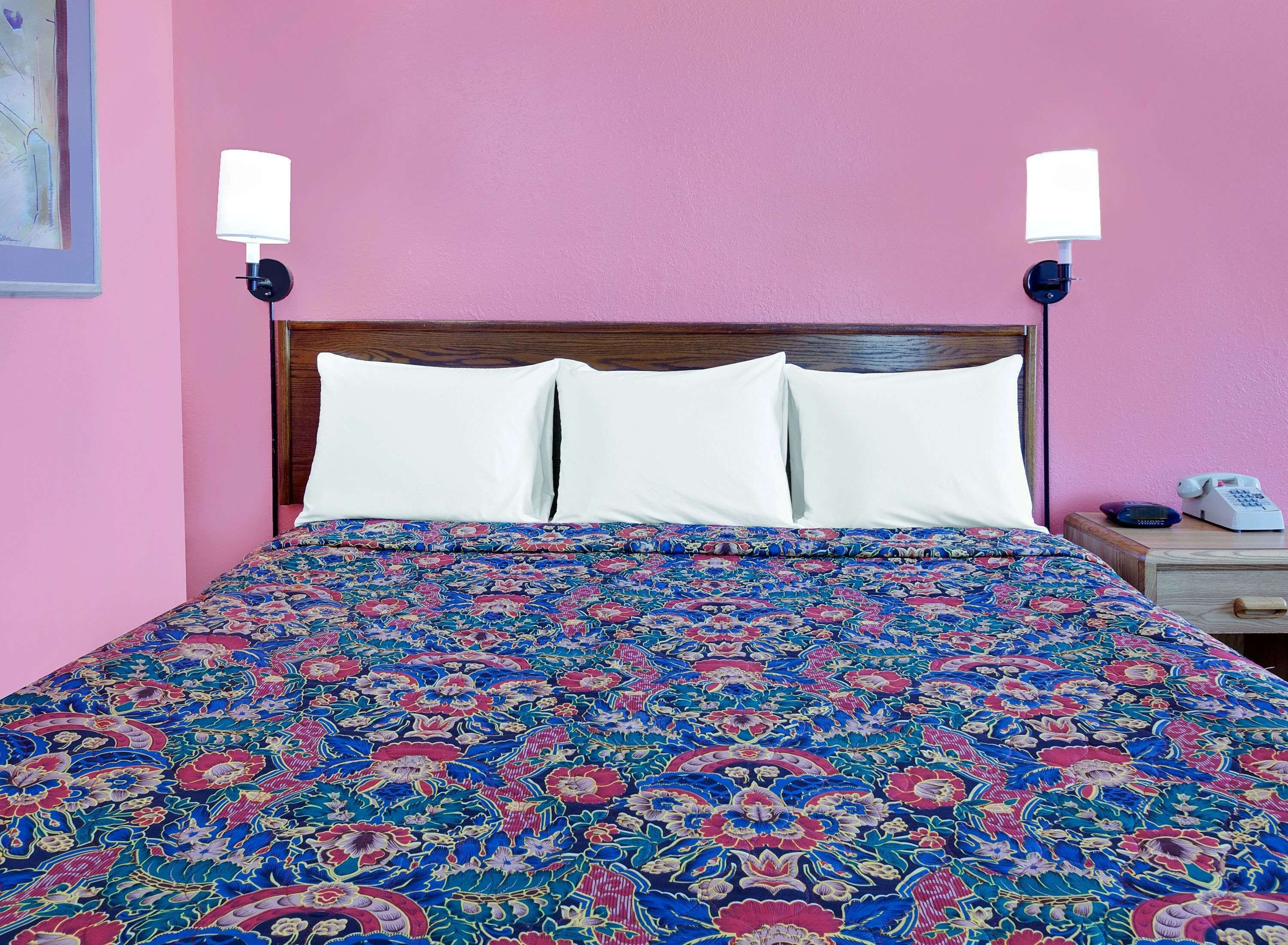 Uma cama com colcha estampada de flores, duas luminárias de cabeceira e uma mesinha de cabeceira com um telefone.