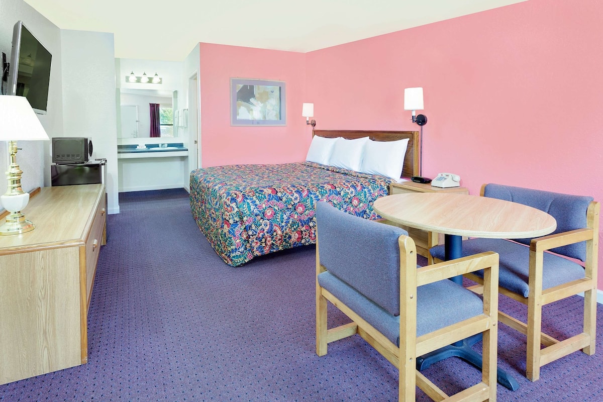 A hotel room with a bed, a desk, a chair, and a table.