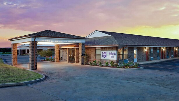 A Knights Inn with a brick facade, covered parking, and a landscaped entrance. - Knights Inn Muskogee (Muskogee)
