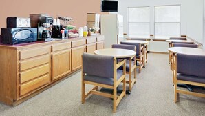 A kitchenette with a microwave, toaster, coffee maker, and a small refrigerator. There are wooden cabinets and a countertop. The room has a carpeted floor and a window with blinds. - Knights Inn Muskogee (Muskogee)