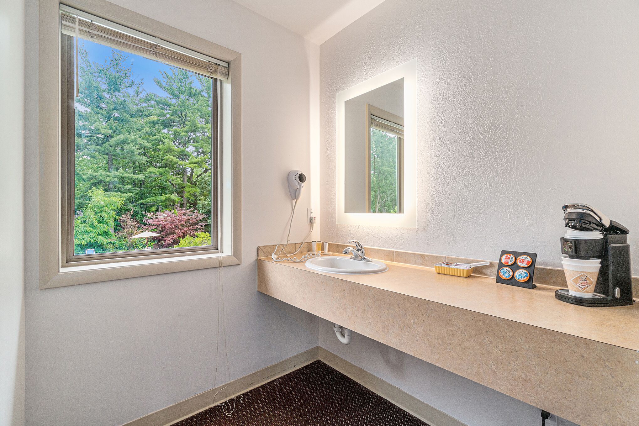 A bathroom with a window, sink, mirror, and coffee maker.