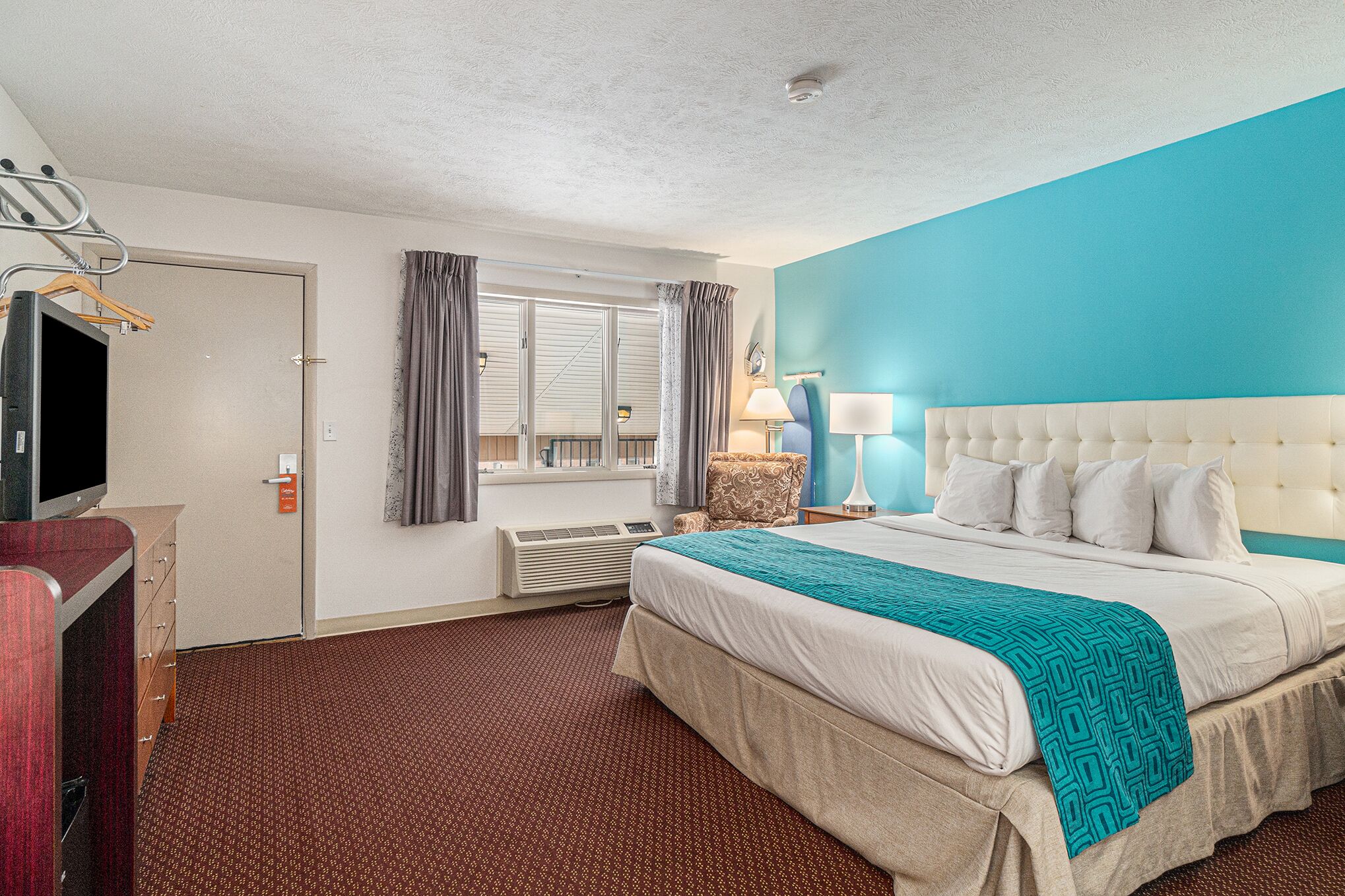 A hotel room with a large bed, a TV, a desk, and a window with curtains.