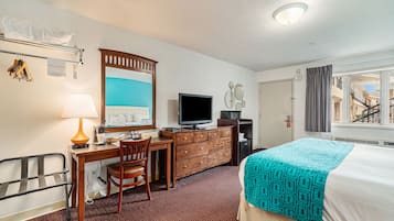 A hotel room with a bed, desk, chair, television, dresser, and a window with a view of a building.