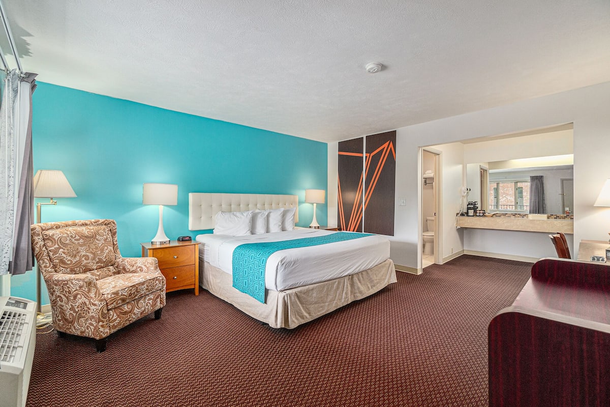 Ein Hotelzimmer mit einem Bett, einem Sessel, einem Schreibtisch und einem durch eine geöffnete Tür einsehbaren Badezimmer.