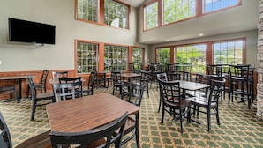 A spacious indoor dining area with multiple tables and chairs, large windows with wooden frames, and a flat-screen TV mounted on the wall.