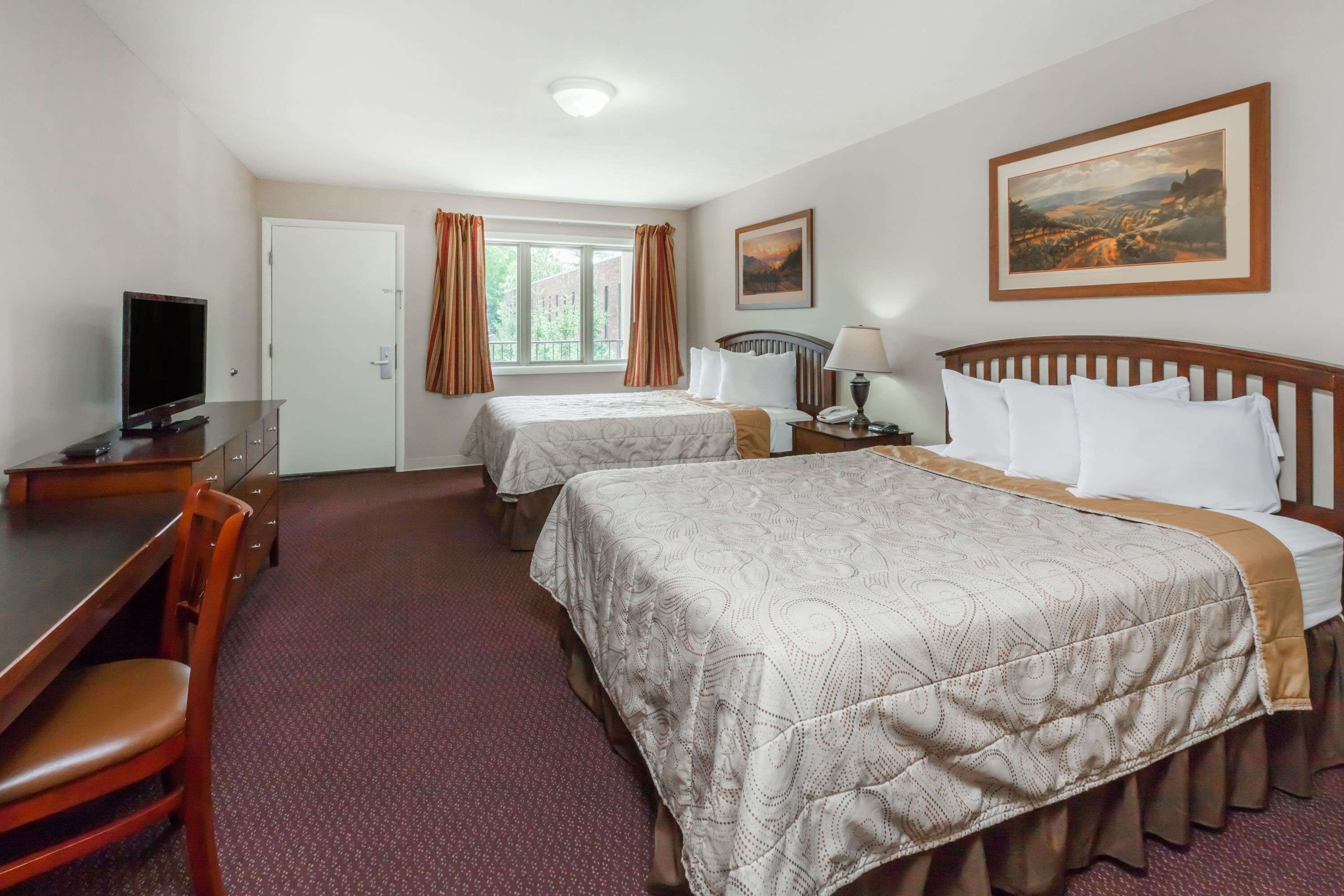 A hotel room with two beds, a desk with a television, a chair, and a window with curtains.