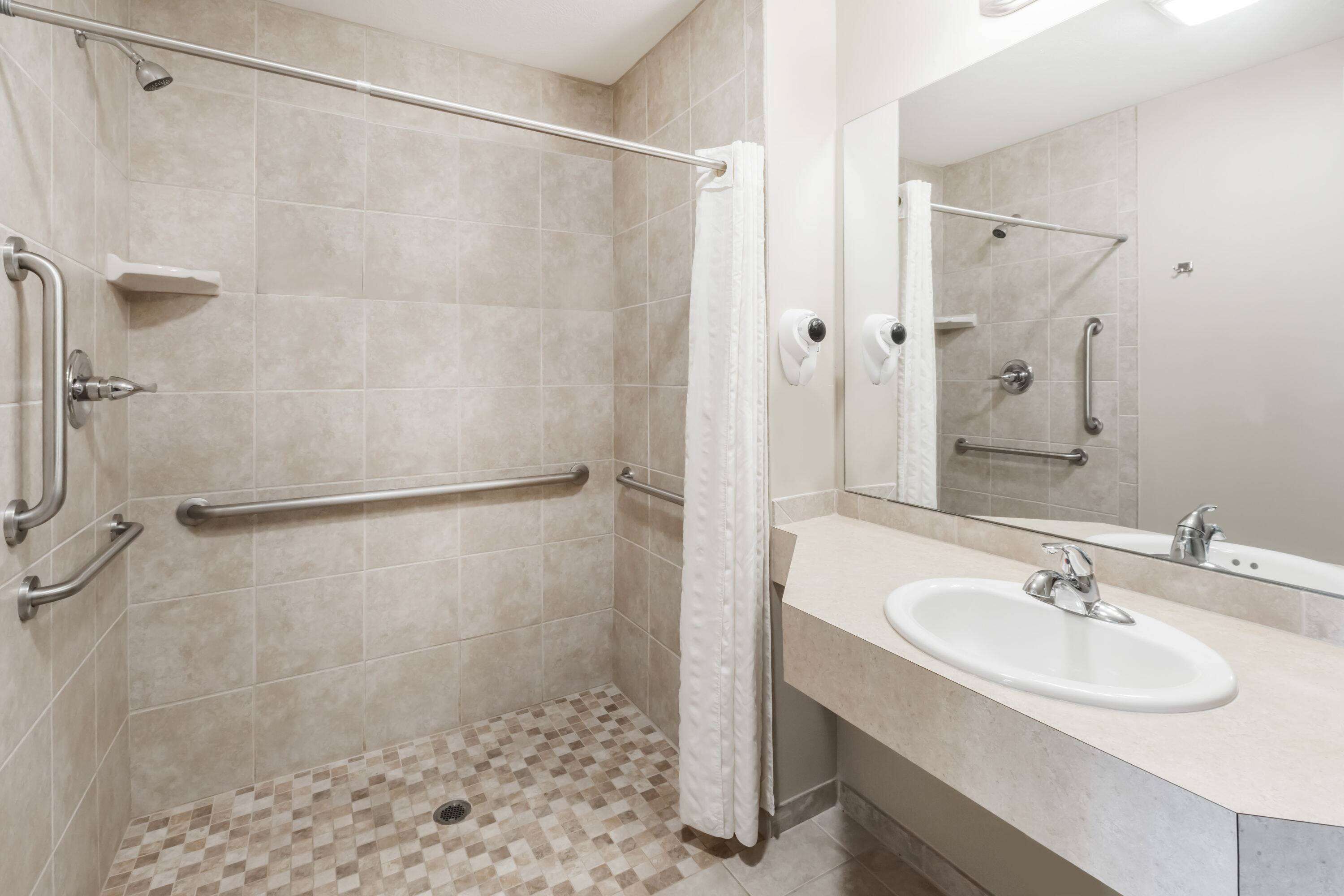 Une salle de bain équipée d’une douche, de barres d’appui, d’un lavabo et d’un miroir.
