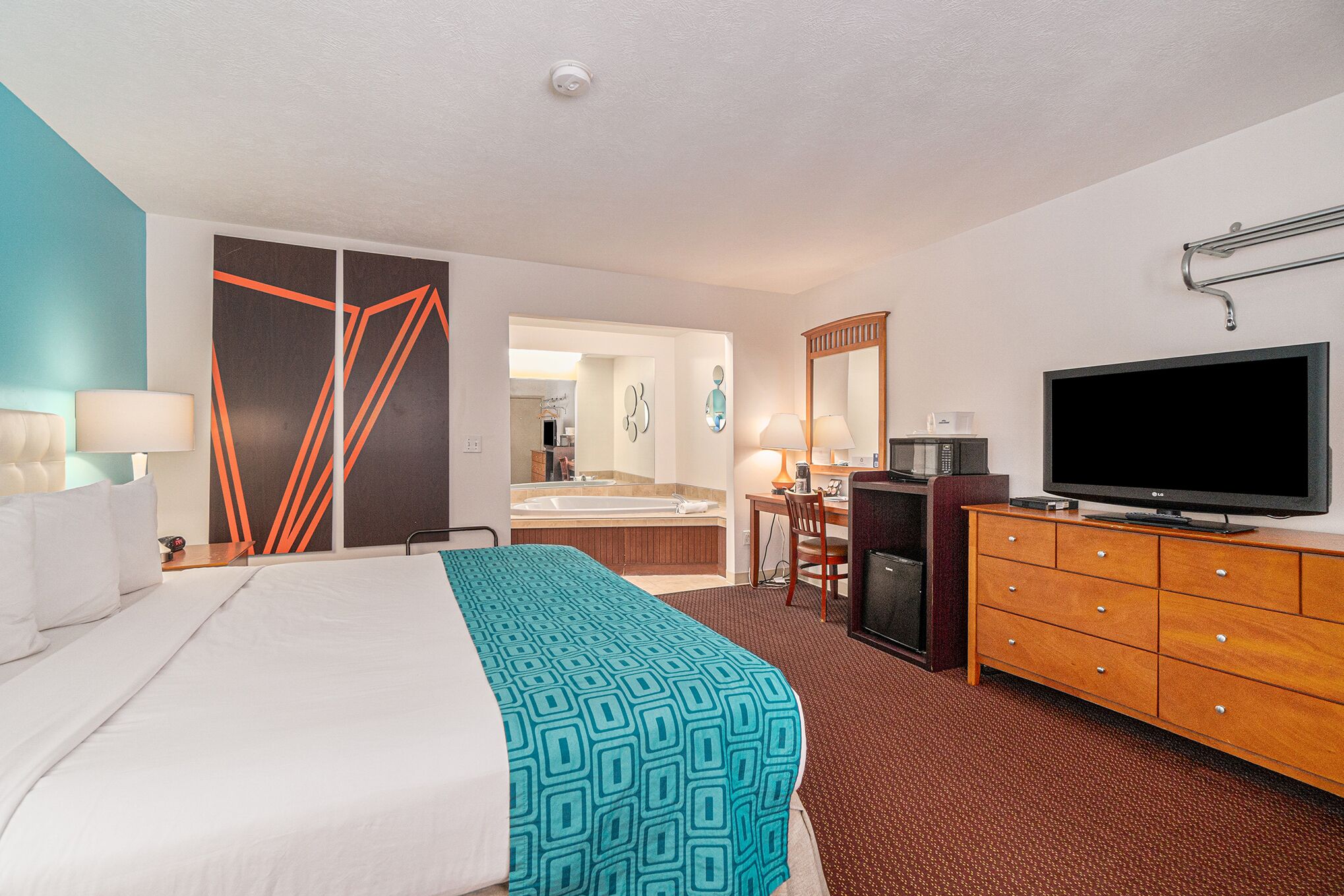 A hotel room with a bed, a TV, a desk, and a bathroom visible through an open door.