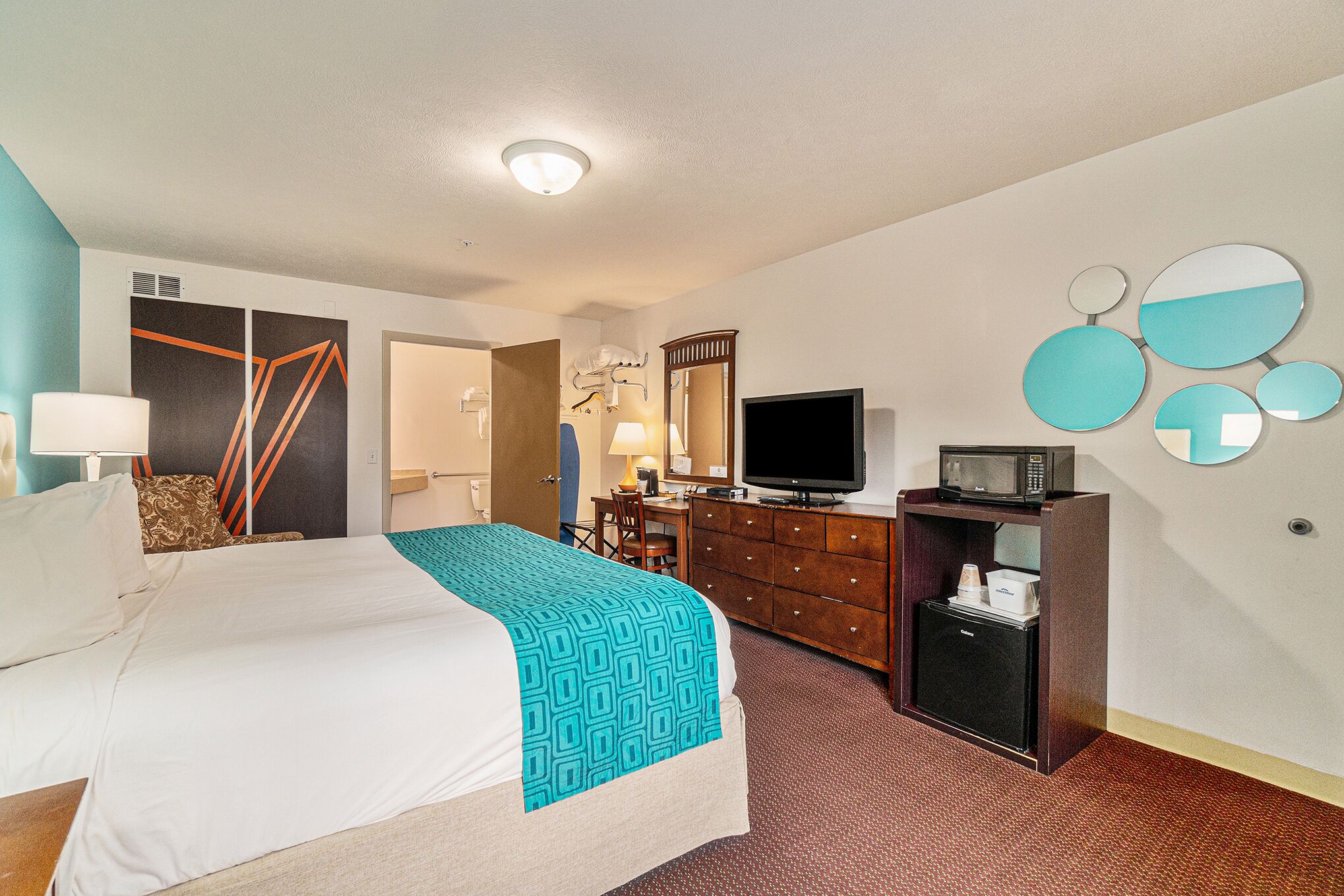 Quarto de hotel com cama, escrivaninha, televisão, micro-ondas e espelho.