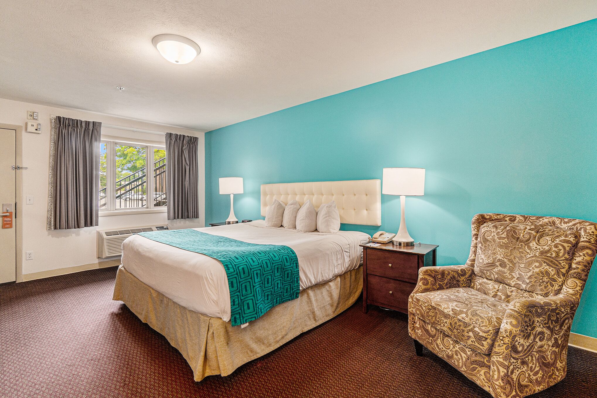 A hotel room with a bed, bedside lamps, a chair, and a window with curtains.