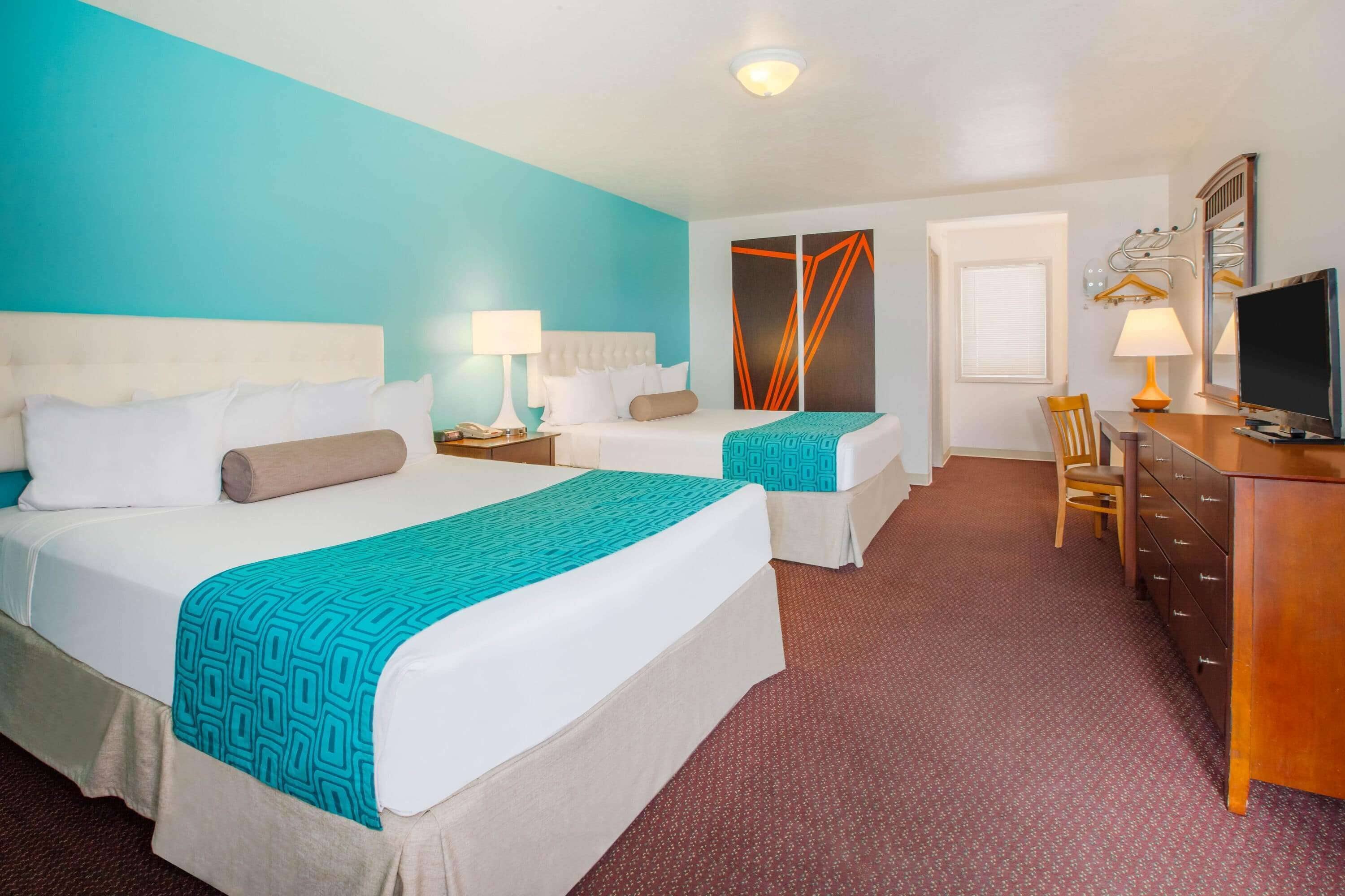 Une chambre d’hôtel avec deux lits, un bureau, une chaise et un téléviseur.