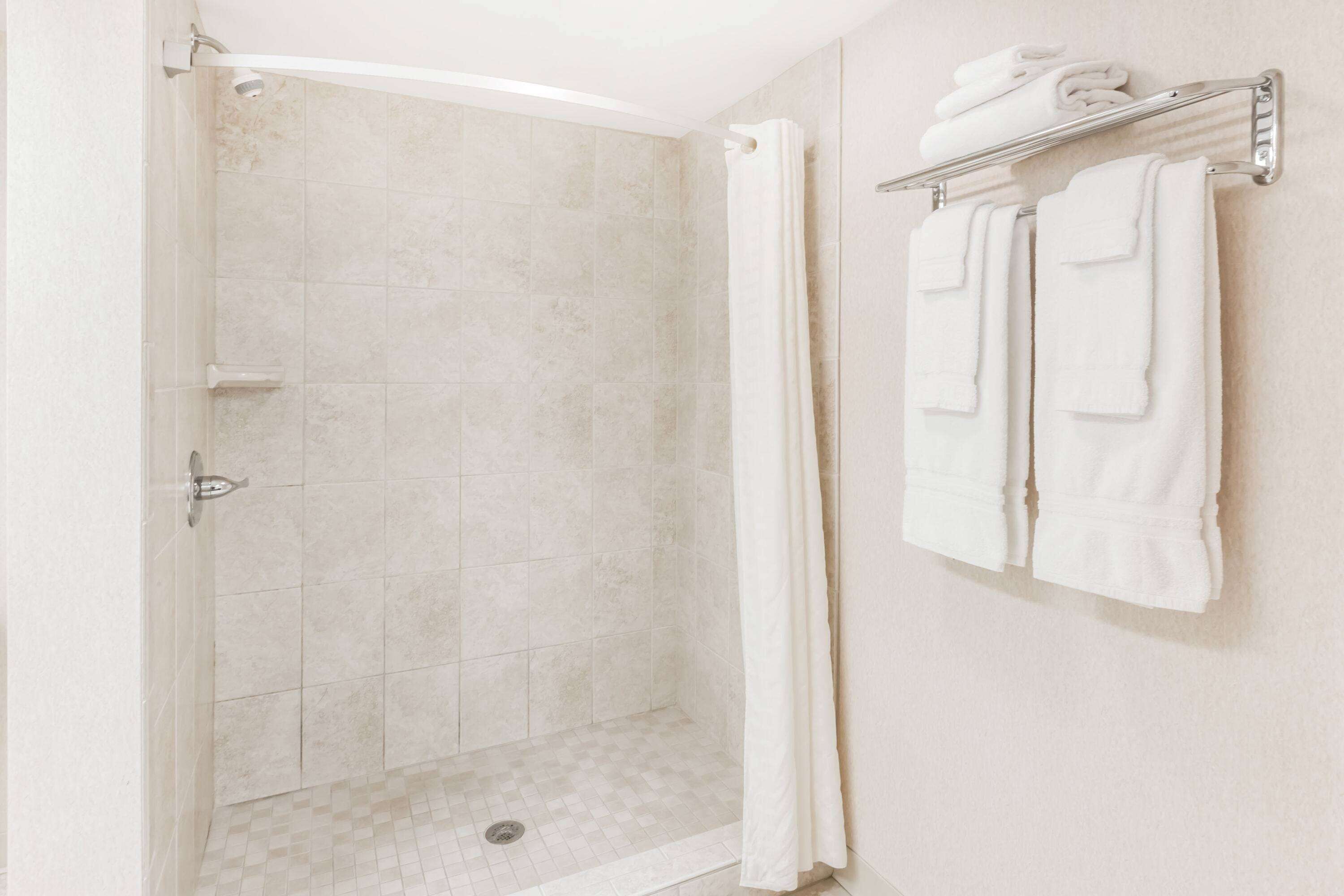 A shower with a glass door, a towel rack with folded towels, and a shower curtain.