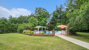 A backyard with a pool, a pergola, and a covered patio area.