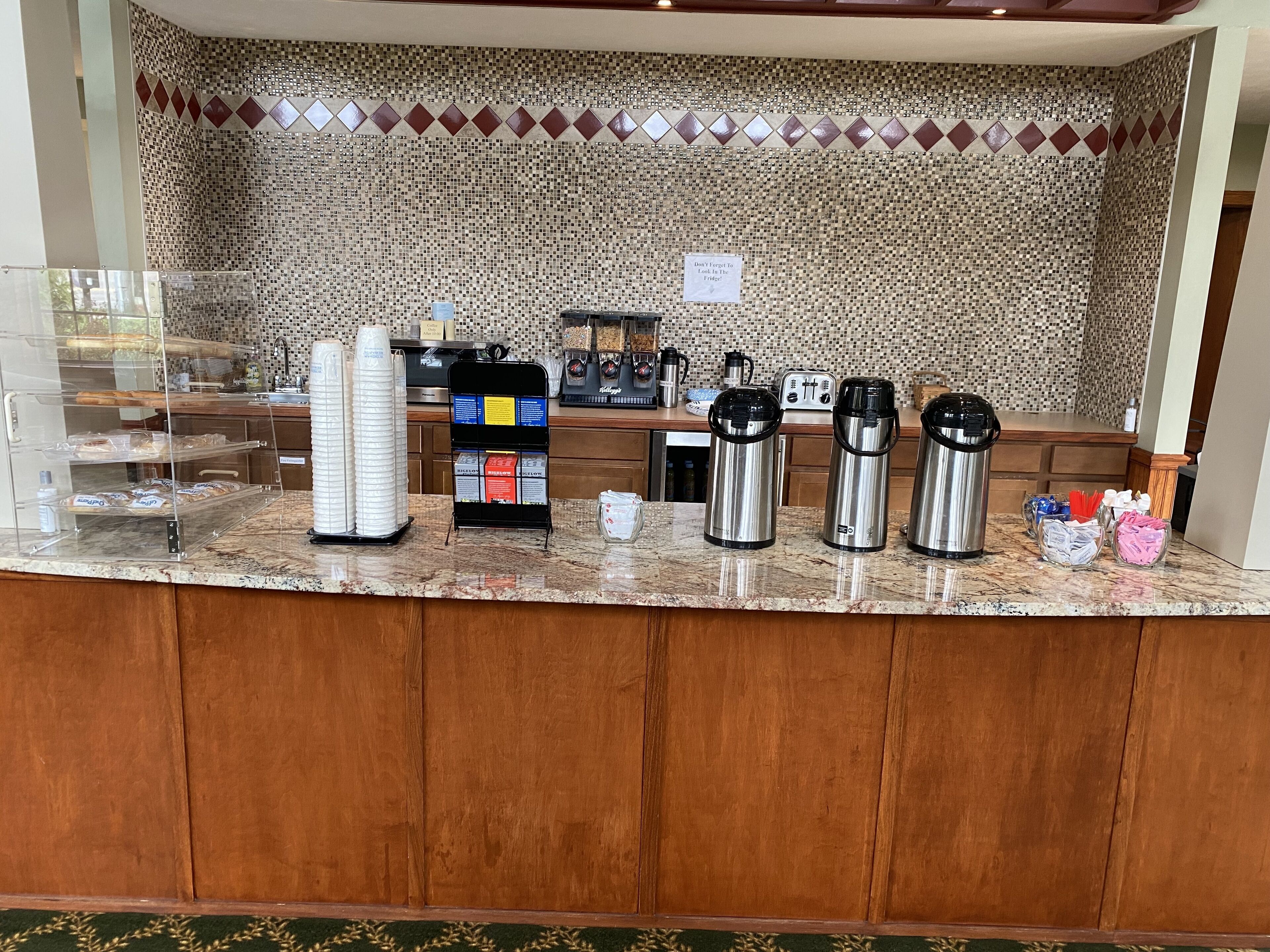 Een ontbijtbalk met een betegelde spatwand, een koffiehoek met drie thermosbekers en een menubord.