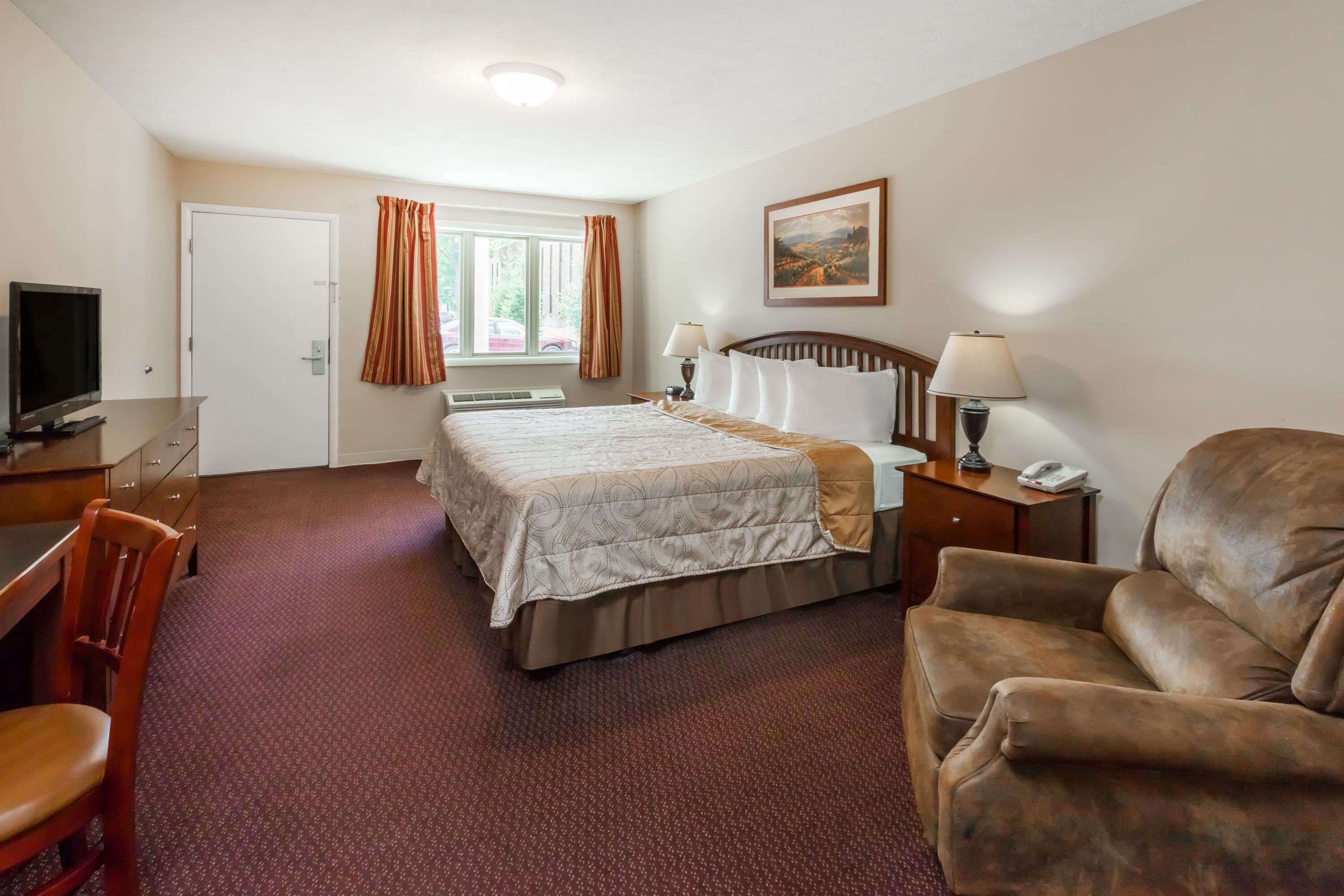A hotel room with a bed, a desk, a chair, a TV, and a window with curtains.