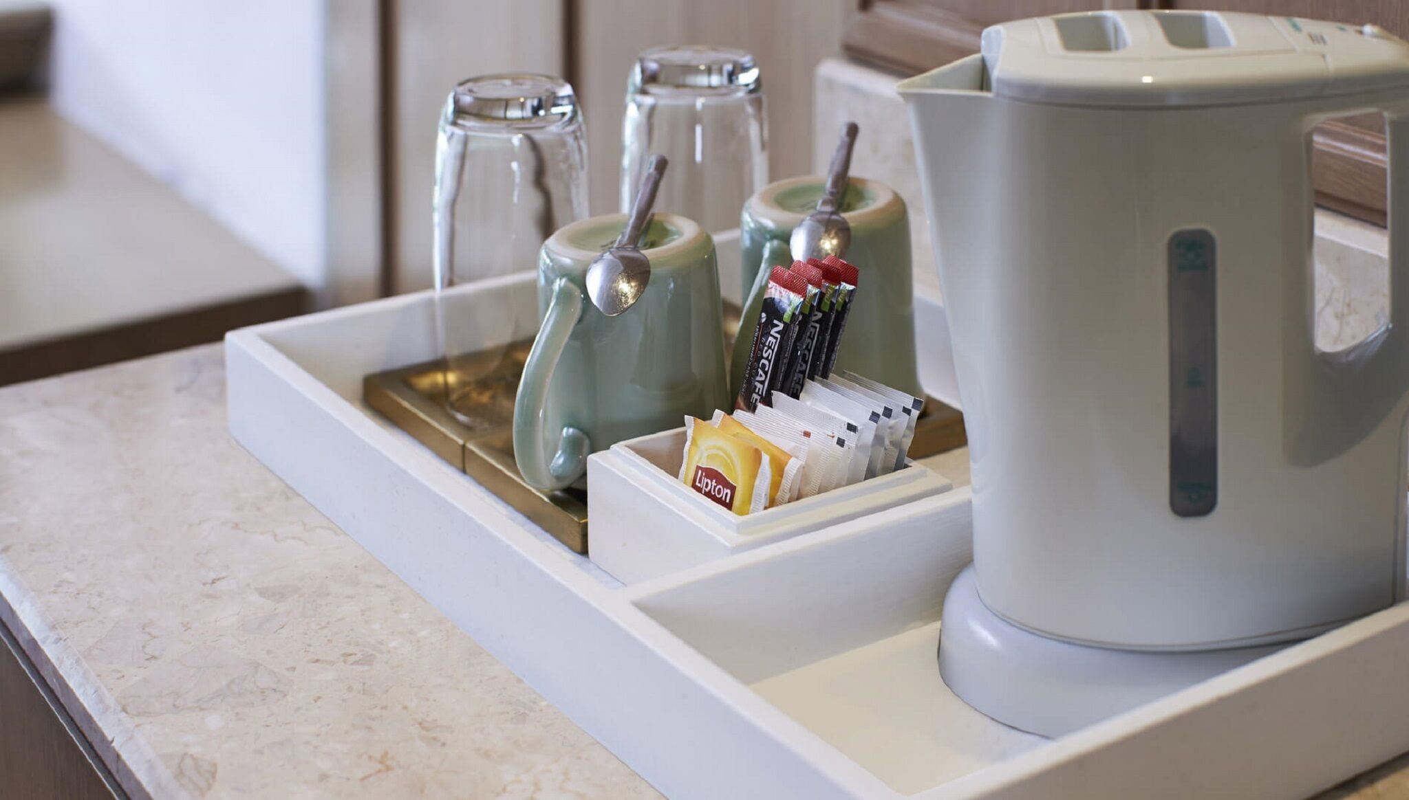 A coffee station with a coffee maker, a tray with a coffee pot, a milk frother, and a Lipton tea packet.