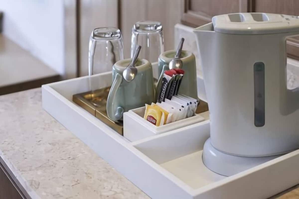 Una encimera de cocina con una cafetera, dos tazas, una bandeja con aderezos y un juego de cuchillos.