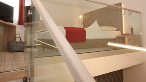 A modern hotel room with a glass partition, a bed with a red blanket, a wooden nightstand, and a handbag on the floor.