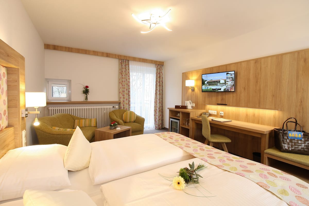 Quarto de hotel com cama, escrivaninha, cadeira, televisão e janela com cortinas.