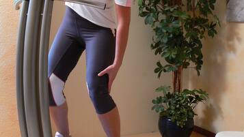 A person using a stationary bike in a room with a large potted plant and a television on the wall.