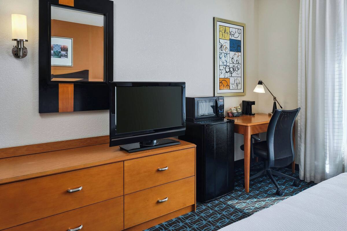 Habitació d'hotel amb un taulell de fusta, un escriptori amb un ordinador, una televisió, una obra d'art abstracta emmarcada i un llit.